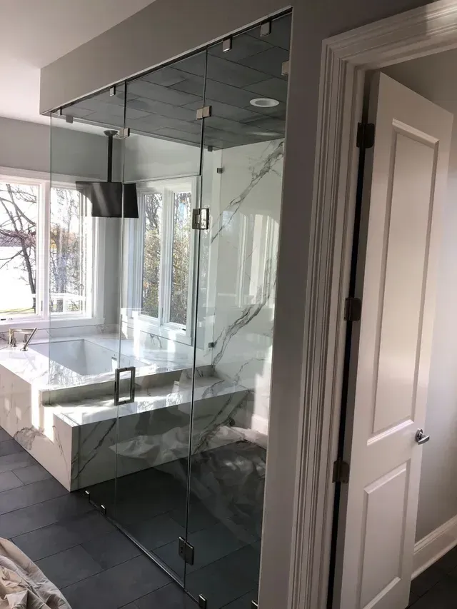 Modern bathroom with glass shower enclosure, marble accents, and a tub near a window.
