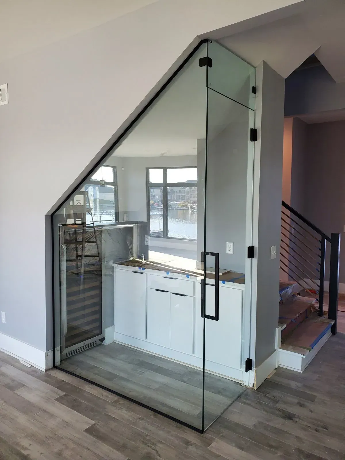 Glass-enclosed wine bar under a staircase. Features a wine fridge, cabinets, and a countertop.