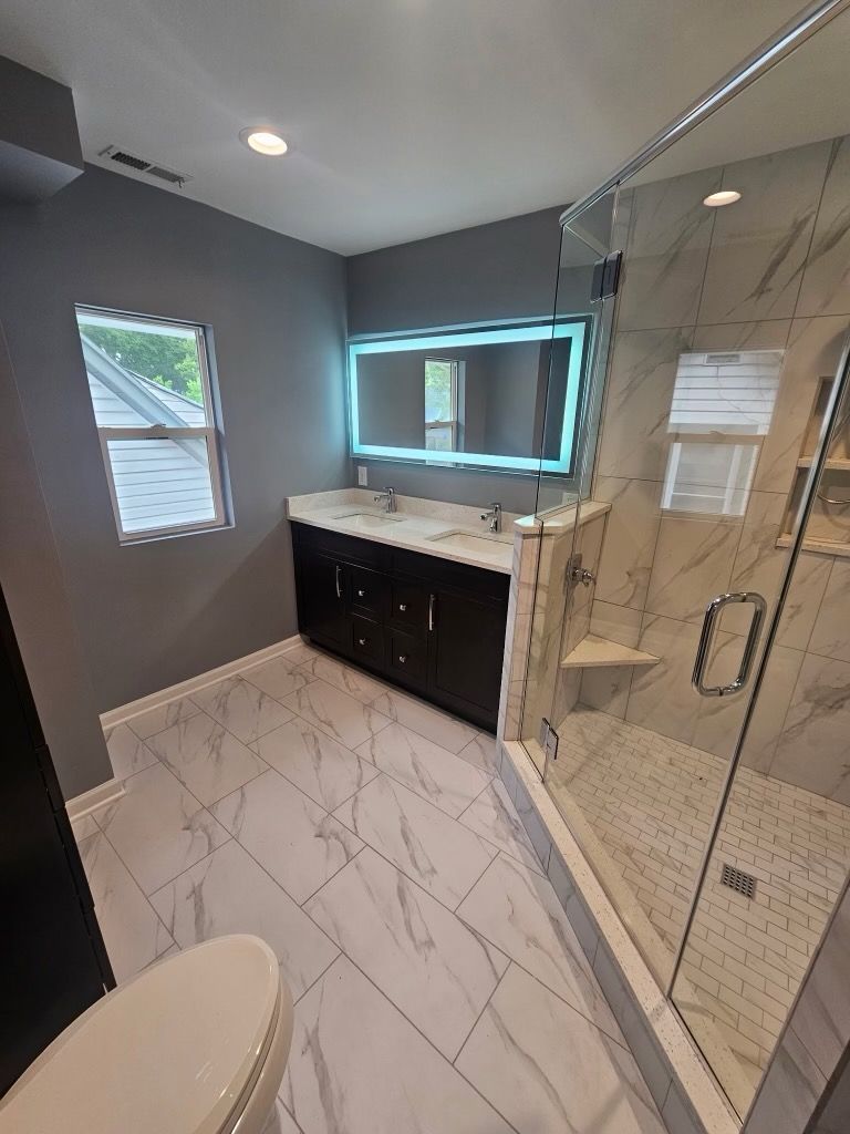 A bathroom with a toilet , sink , shower and mirror.