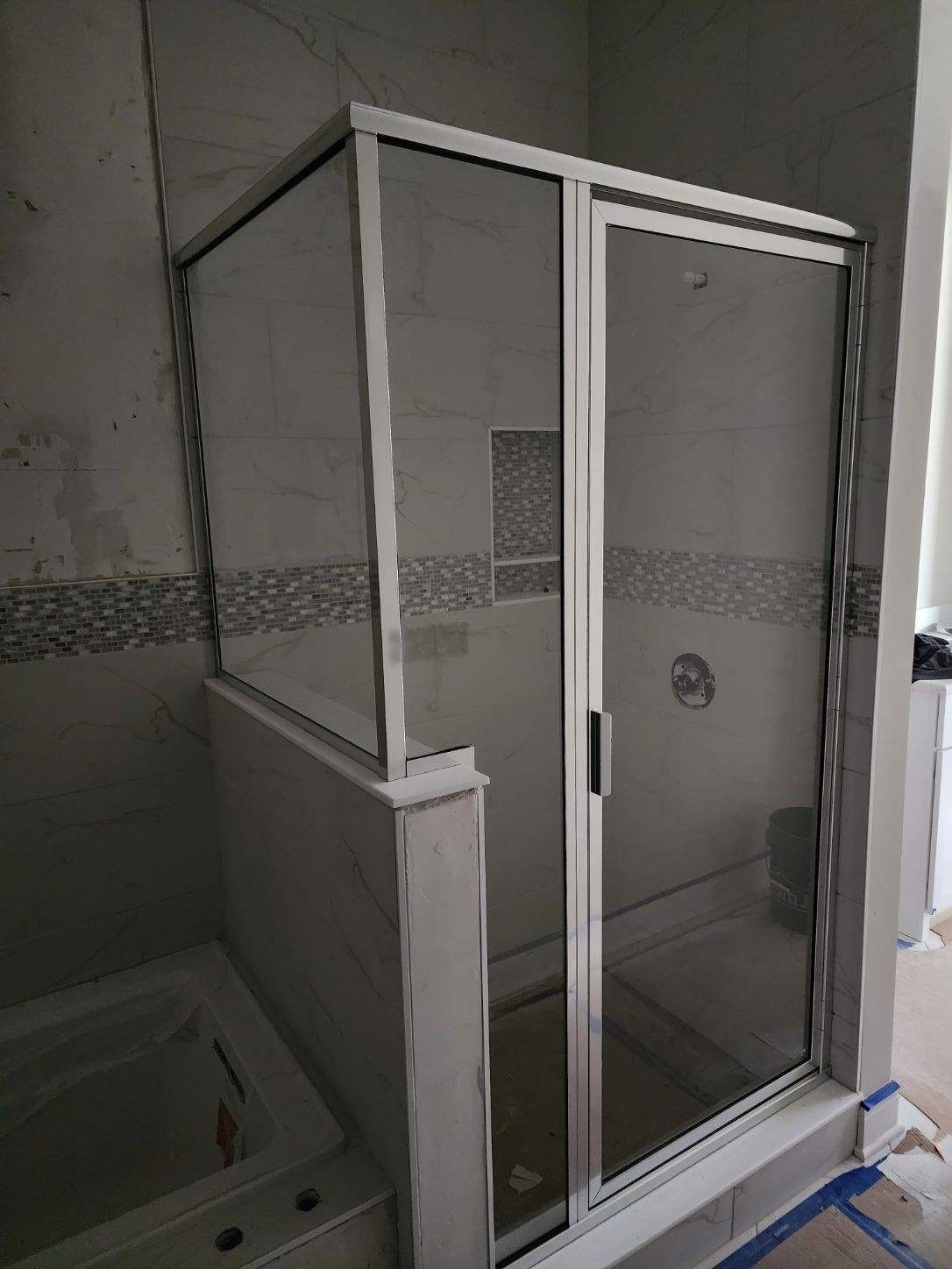 Shower enclosure with sliding glass door, silver frame, installed in a bathroom with tiled walls.