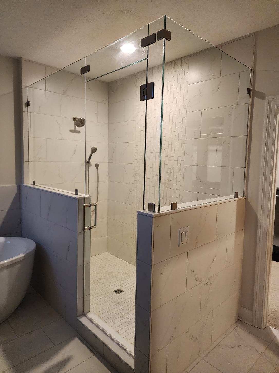 Modern walk-in shower with clear glass panels and gray tile walls. Chrome fixtures, including a shower head and door handle.
