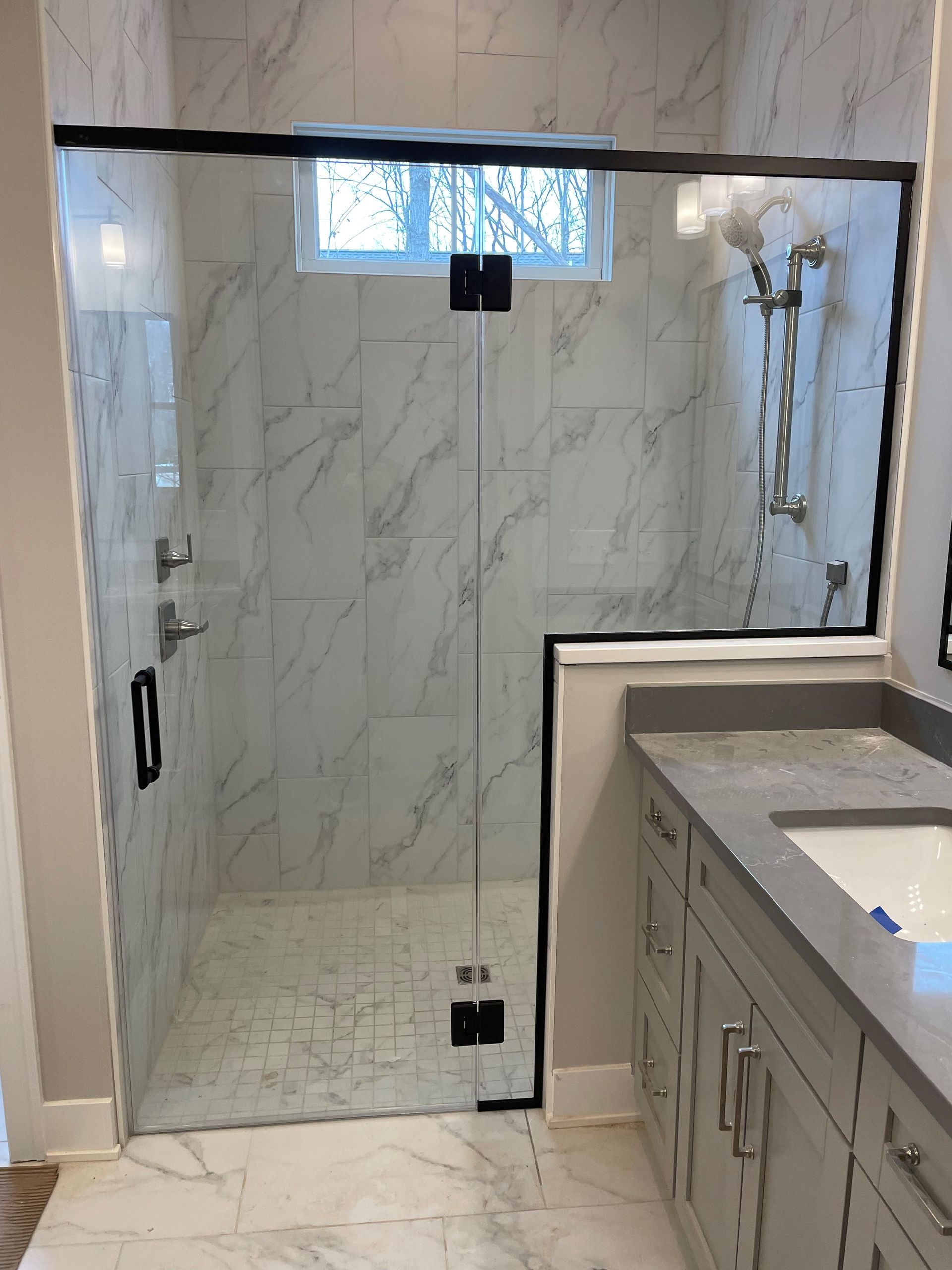 Modern bathroom with marble tile, glass shower door, and gray vanity.
