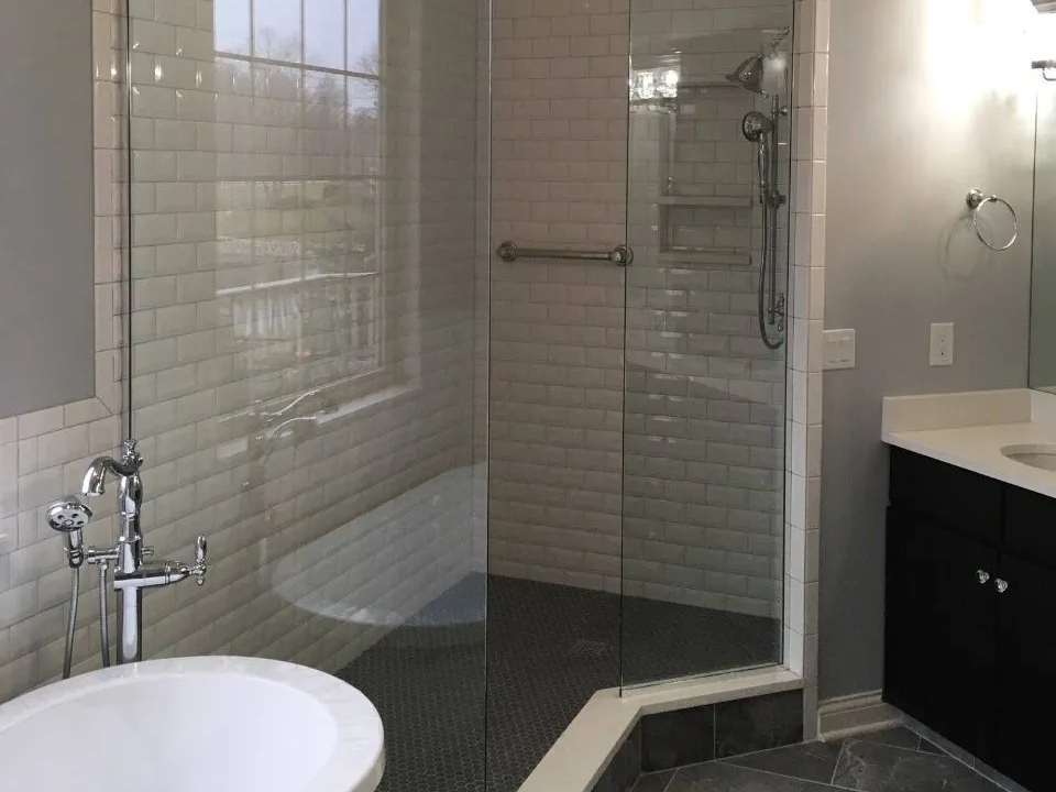 Bathroom with a glass shower enclosure and a freestanding tub. The shower has a grab bar and dark floor tiles.