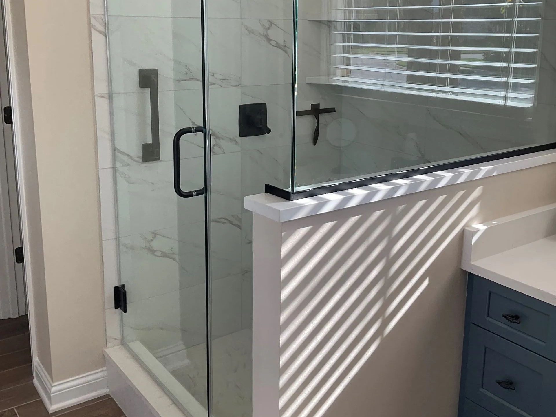 Glass shower enclosure with black hardware, white tile, and blue vanity.