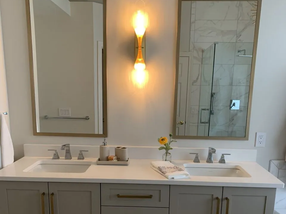 Bathroom with dual sinks, mirrors, and a decorative light fixture. Light gray cabinets, white countertop.