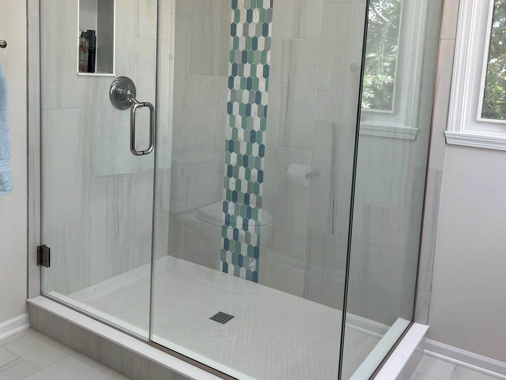 Glass shower with white and blue tile accents, silver fixtures.