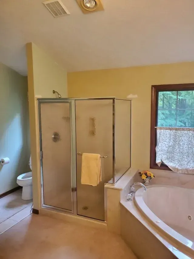 Bathroom with shower, toilet, and jacuzzi tub. Yellow walls, glass shower door, and a towel.