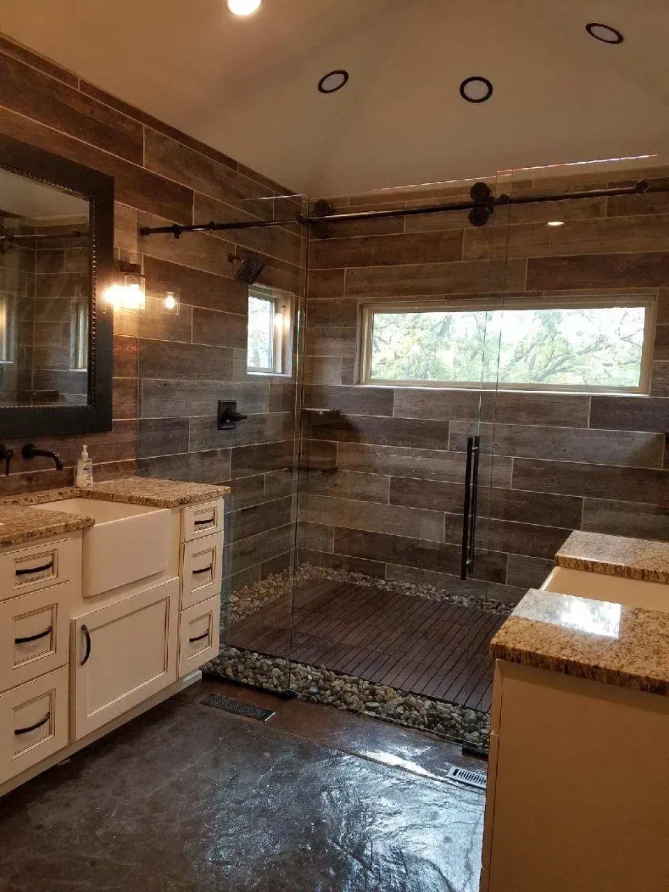 Bathroom with wood-look tile, glass shower, stone flooring, white cabinets, and a large window.