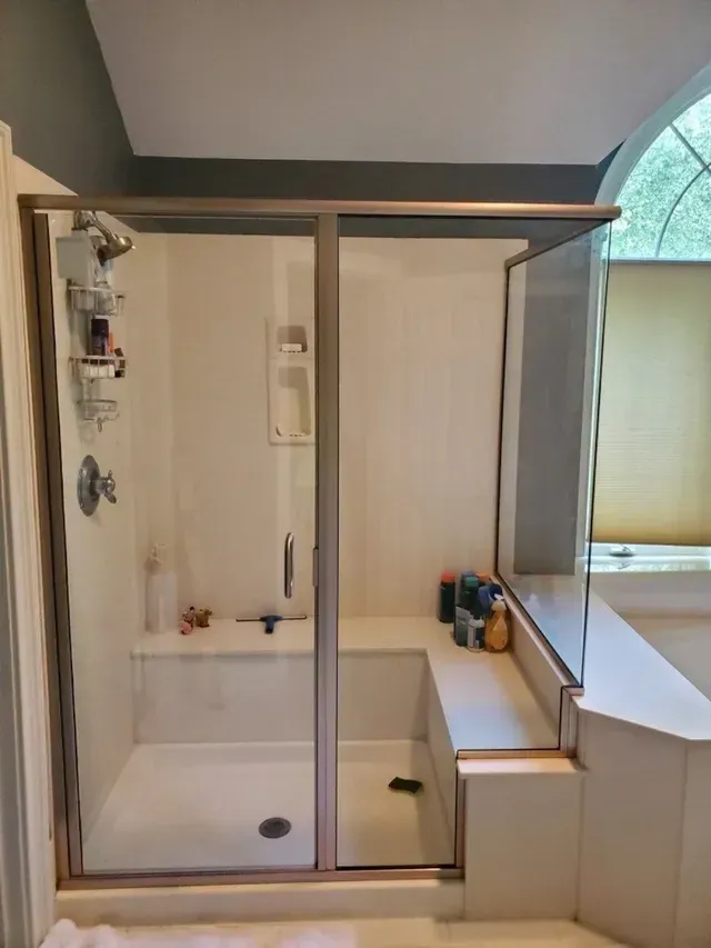 A shower enclosure with a sliding door and a built-in bench, next to a bathtub.