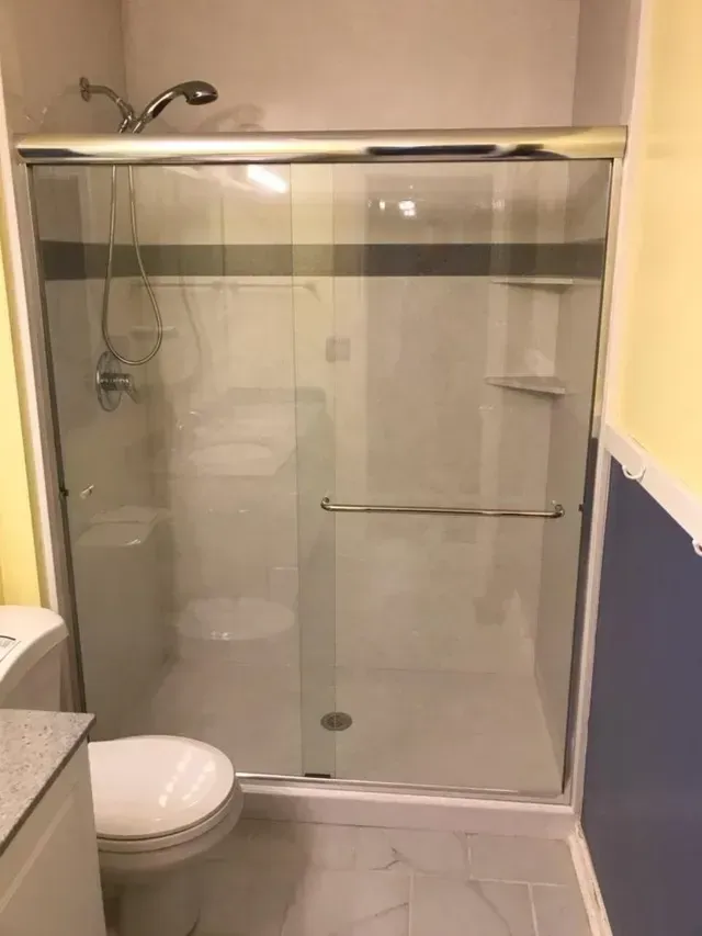 Bathroom with sliding glass shower door, toilet, and shower head visible. Gray and white color scheme.