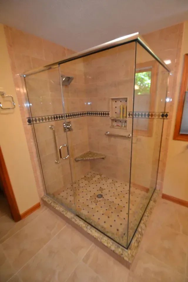 Glass shower enclosure with tiled walls, stone floor, and built-in shelves.