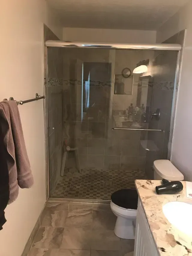 Bathroom with glass shower, toilet, vanity. Towel rack on the left.