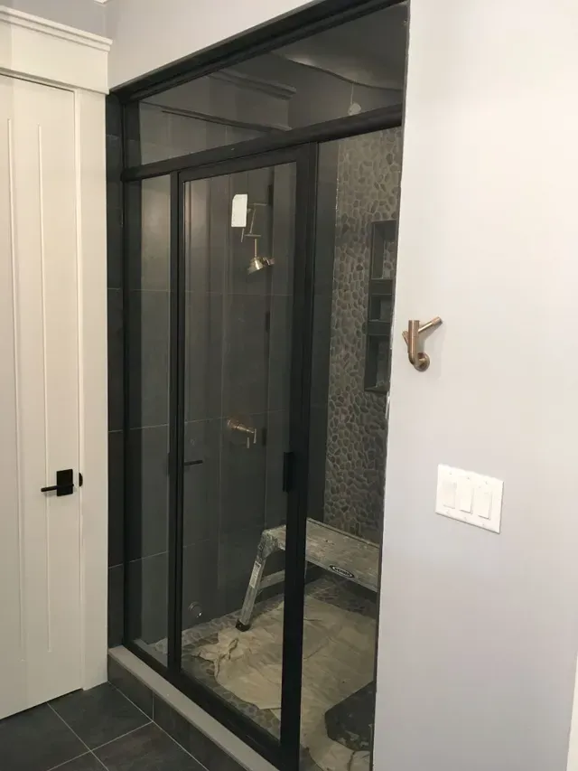 Modern shower with black-framed glass doors, adjacent to a white door and gray wall.