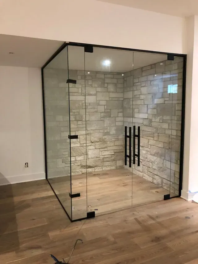 Glass-enclosed room with black framing, stone tile wall, and wooden floor. Black handle on the door.