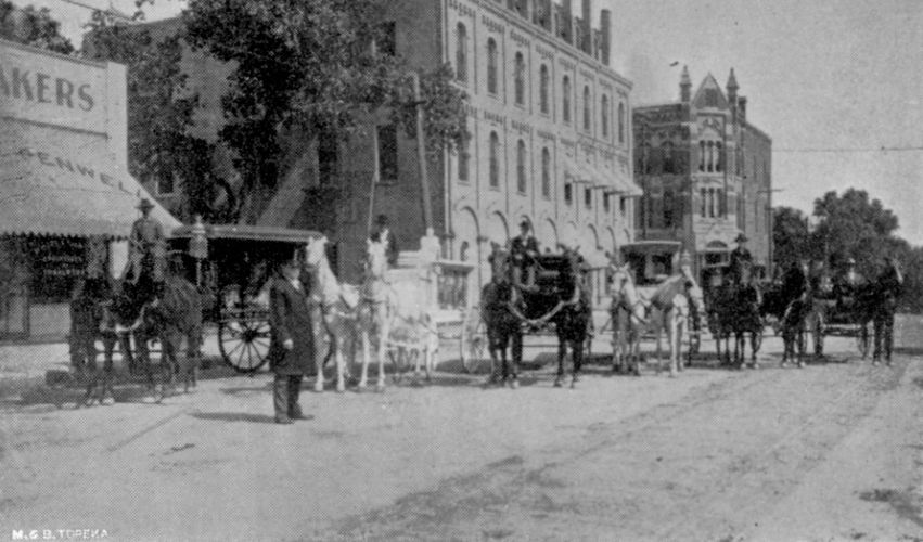 A black and white photo of horse drawn carriages on a city street