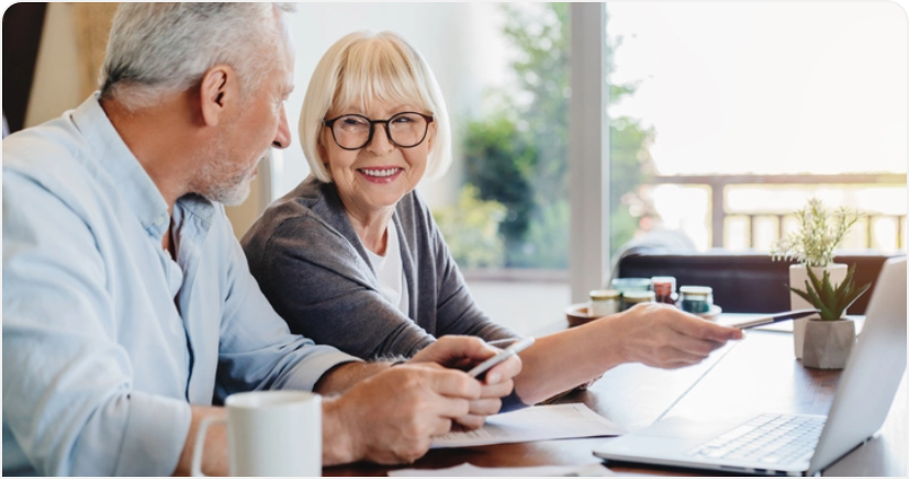 A man and a woman are sitting at a table looking at a laptop.