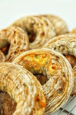 Close-up of a pile of rustic, crusty, golden-brown bread rings on a wire rack.