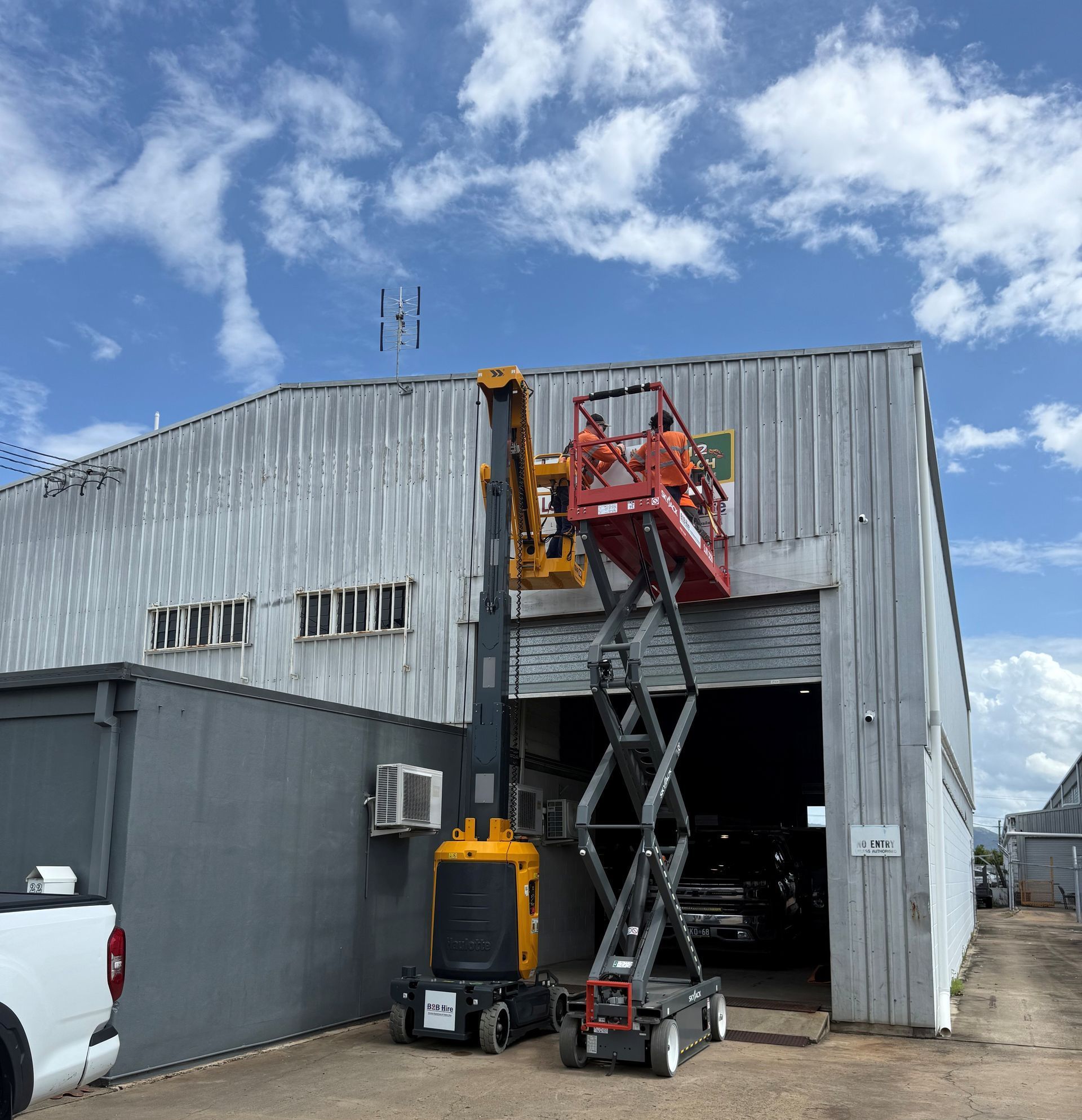 A Man Is Standing On A Scissor Lift In Front Of A Building — B2B Hire In Garbutt, QLD
