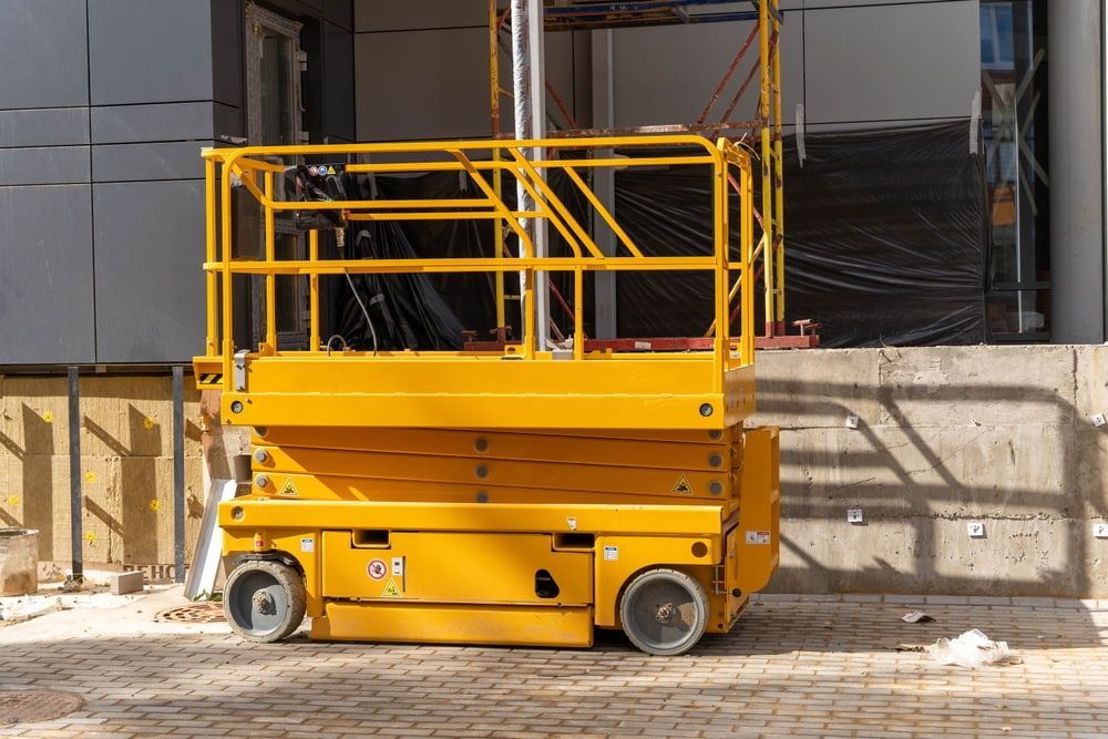 A Yellow Scissor Lift Is Parked In Front Of A Building Under Construction — B2B Hire In Garbutt, QLD