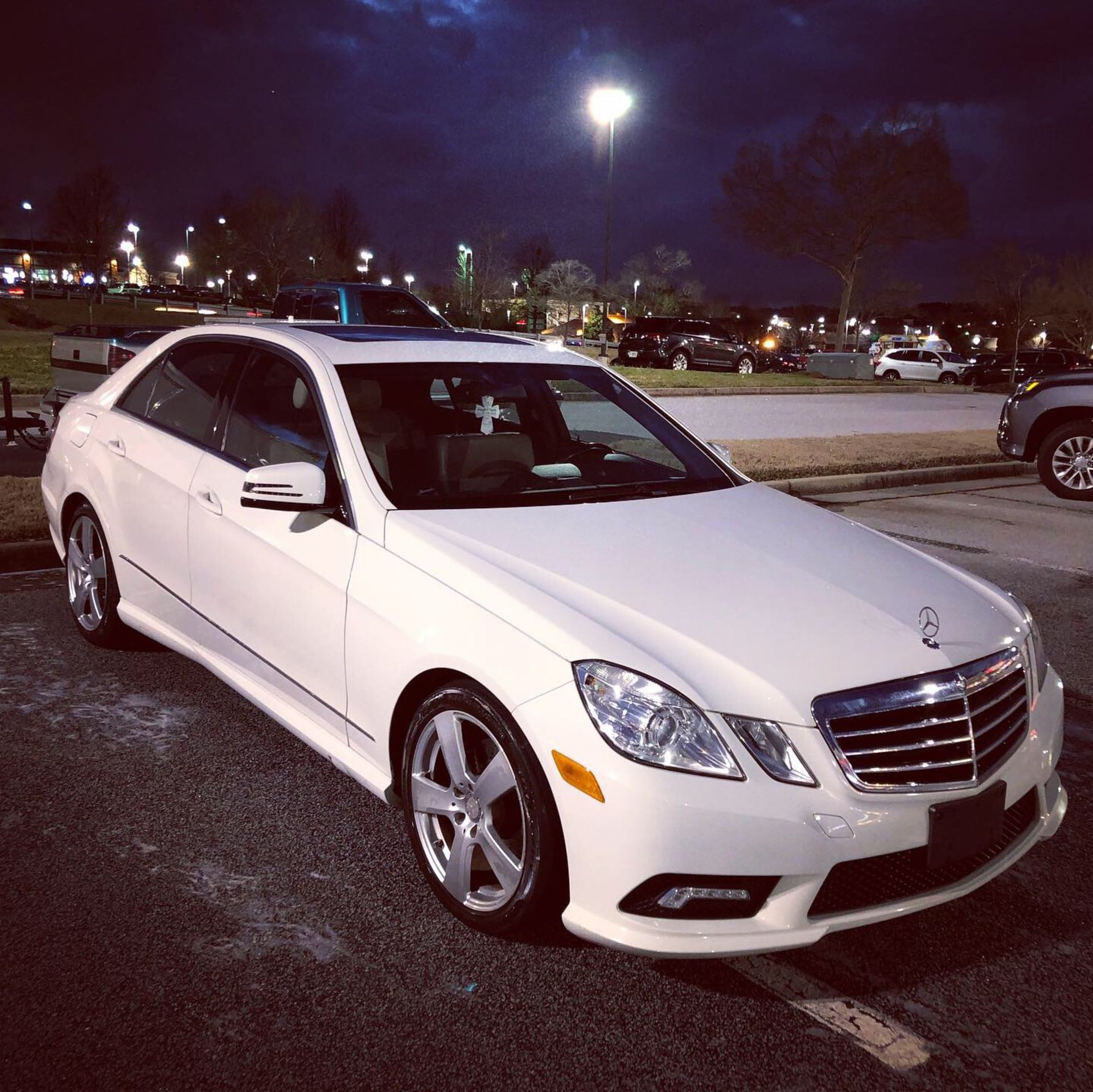 A white mercedes is parked in a parking lot at night
