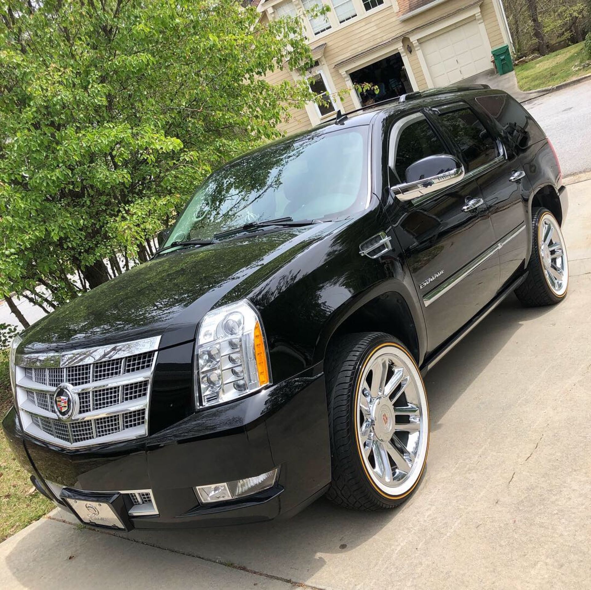 A black cadillac escalade is parked in a driveway in front of a house.