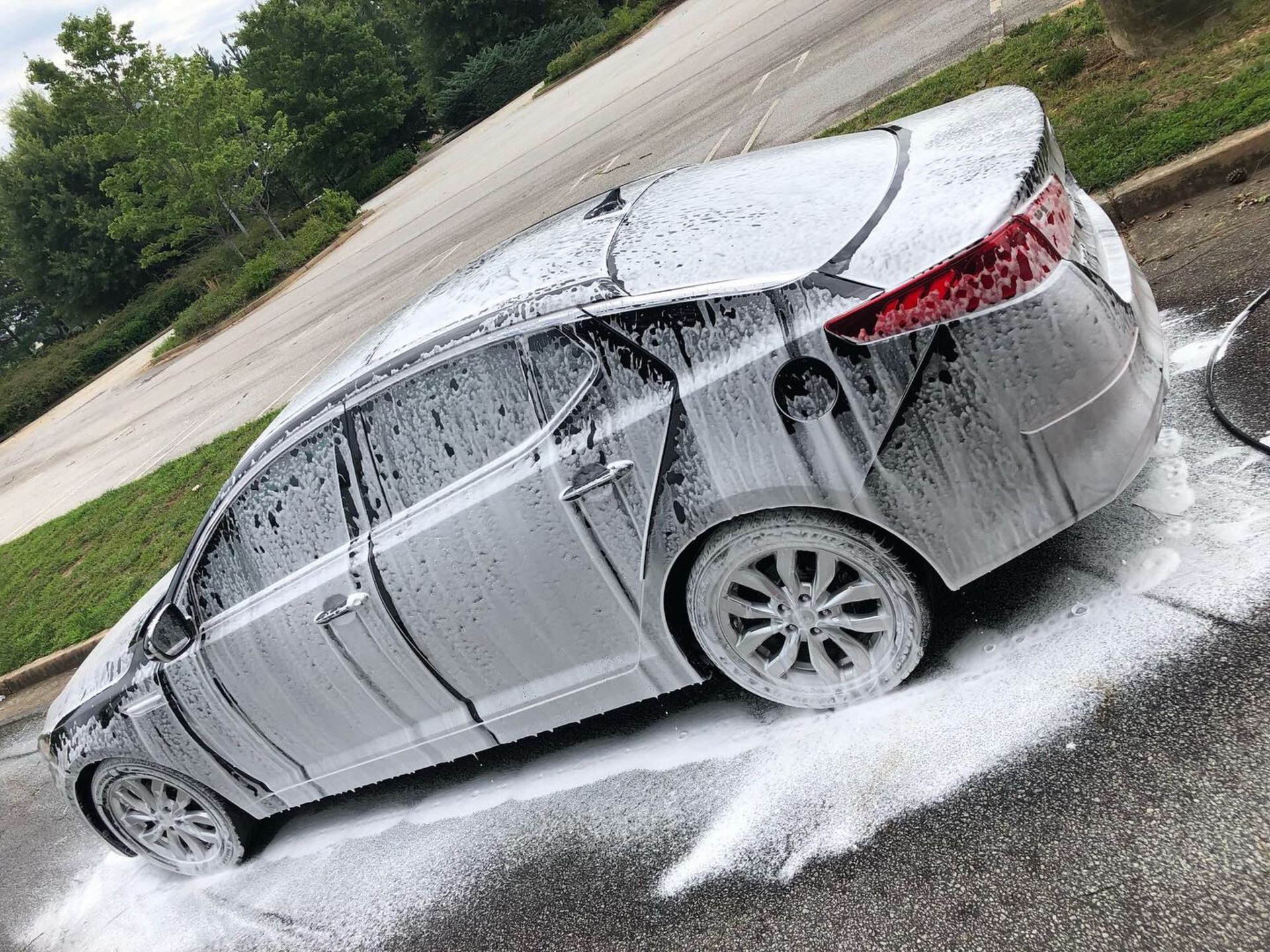 A silver car is covered in foam in a parking lot.