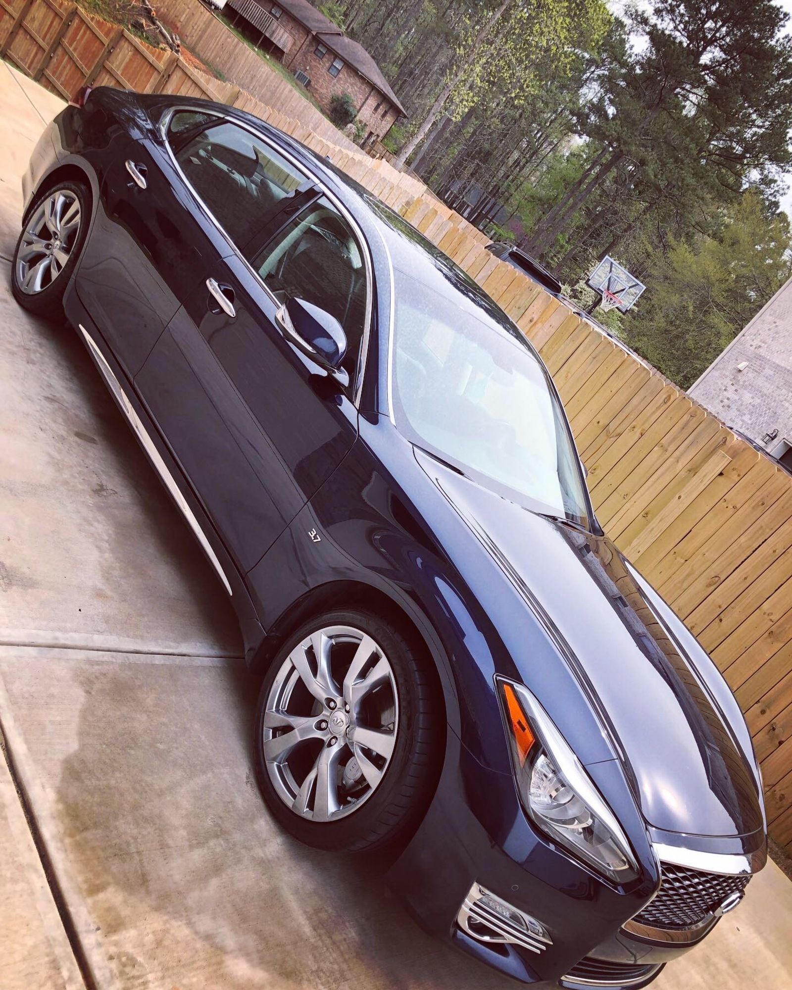 A blue car is parked in a driveway next to a wooden fence.