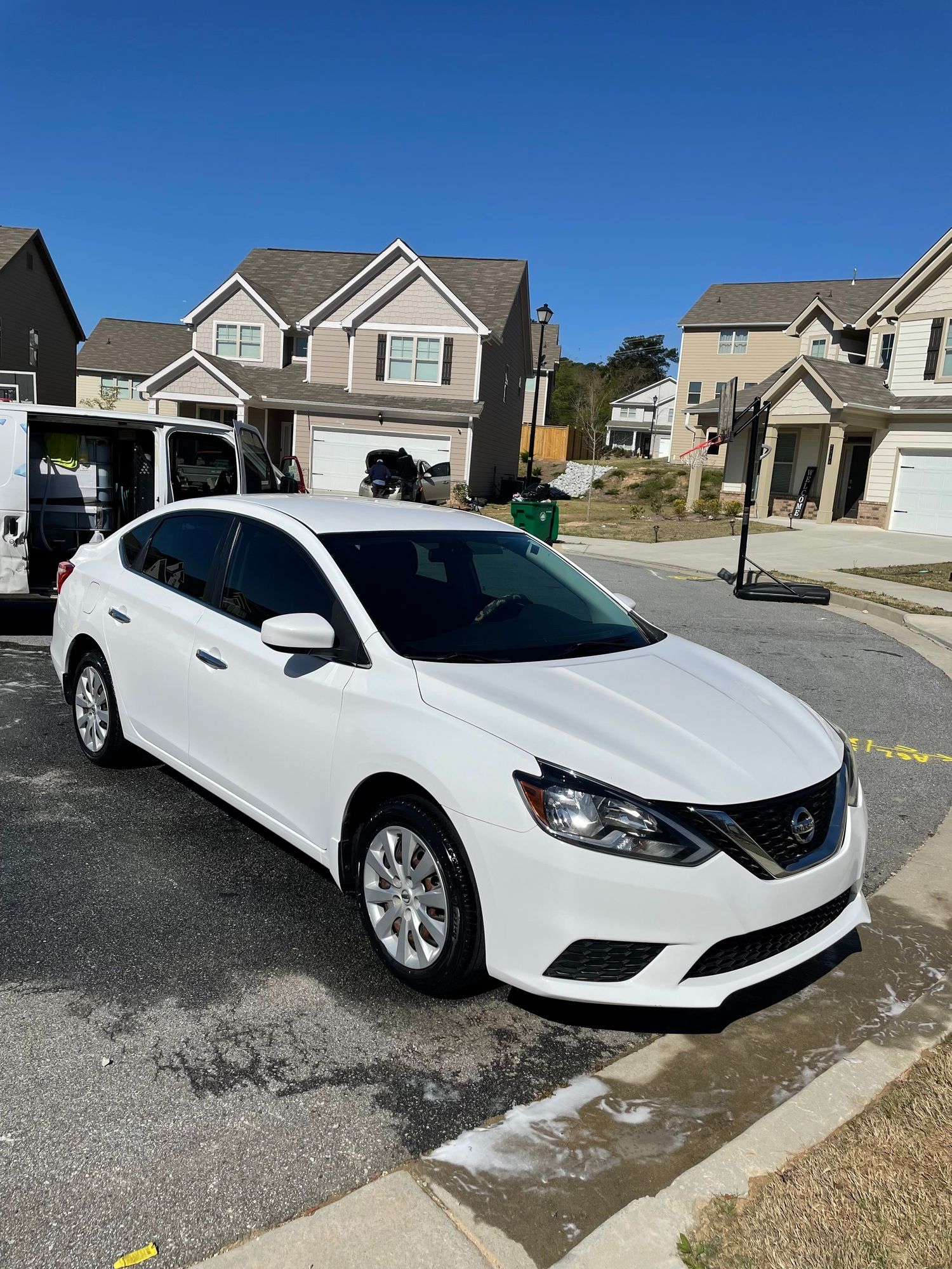 A white car is parked in a parking lot in front of a house.