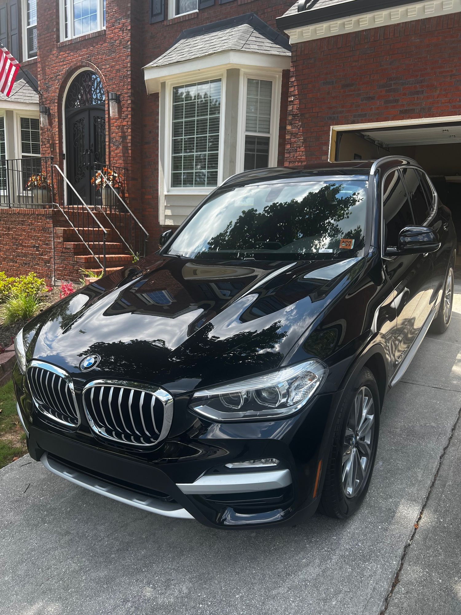A black bmw x3 is parked in front of a brick house.