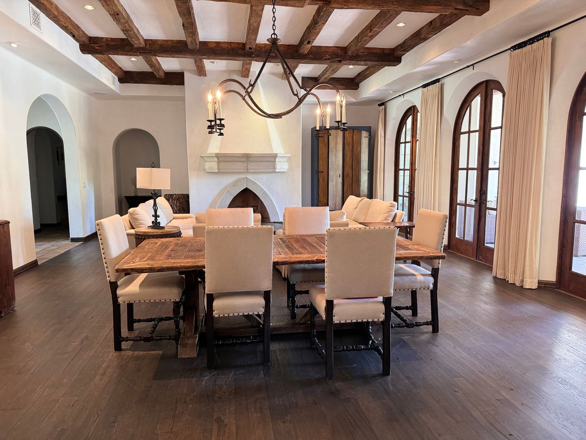 Dining room with wooden ceiling beams, large table, chairs, and arched windows.