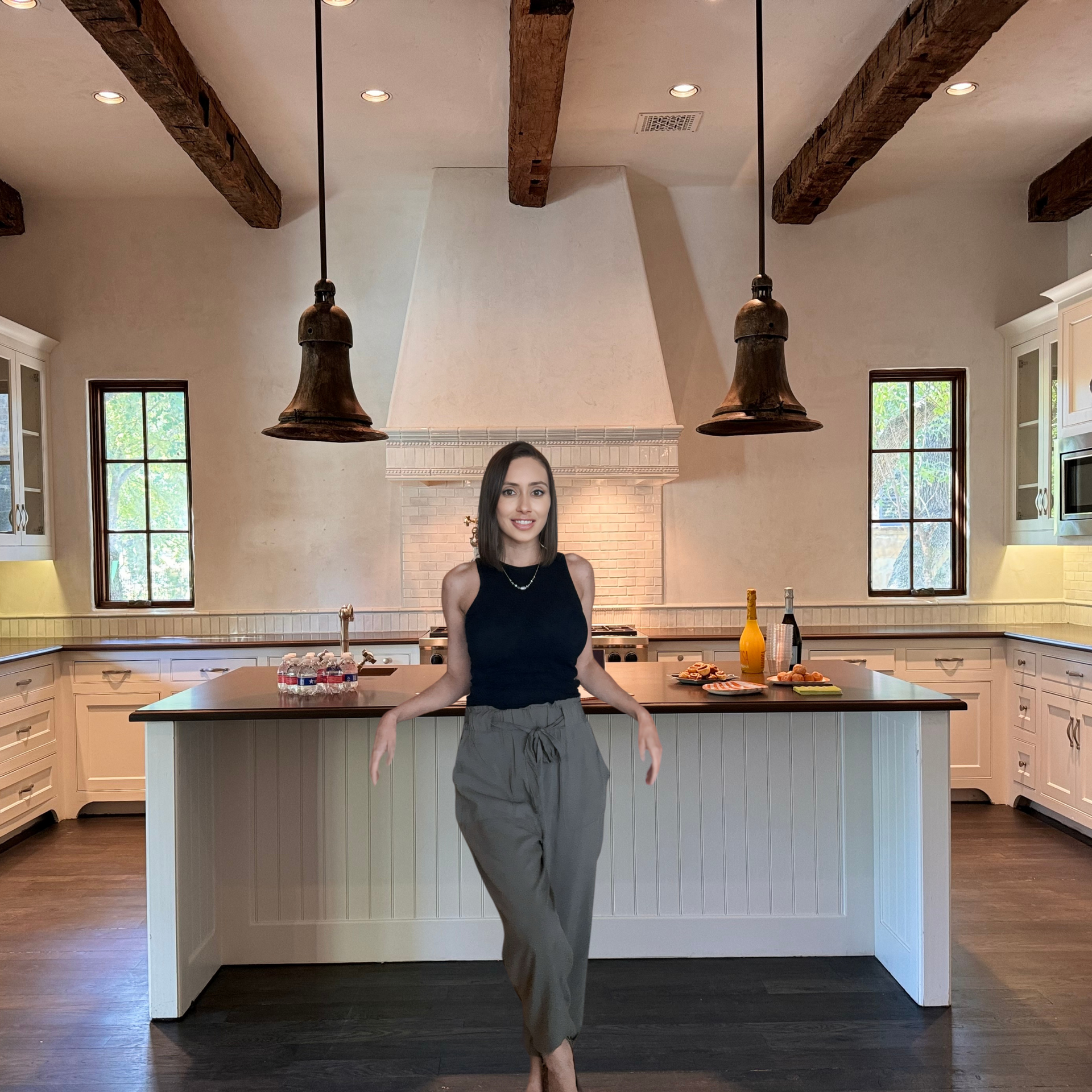 Woman standing in kitchen with dark island and hanging lights.