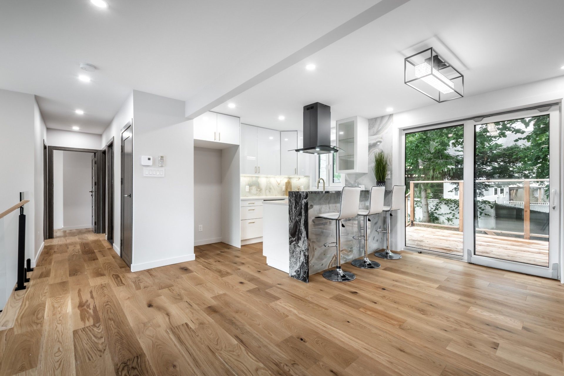 Modern kitchen with hardwood floors, white cabinets, island with stools, and sliding glass doors to a deck.