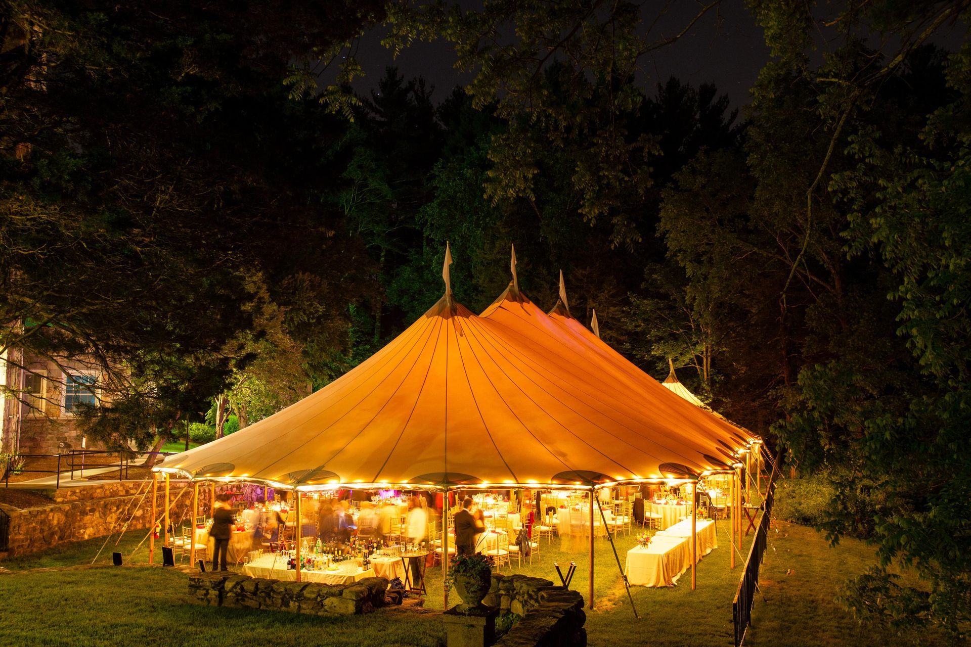 a large tent is lit up at night with tables and chairs inside