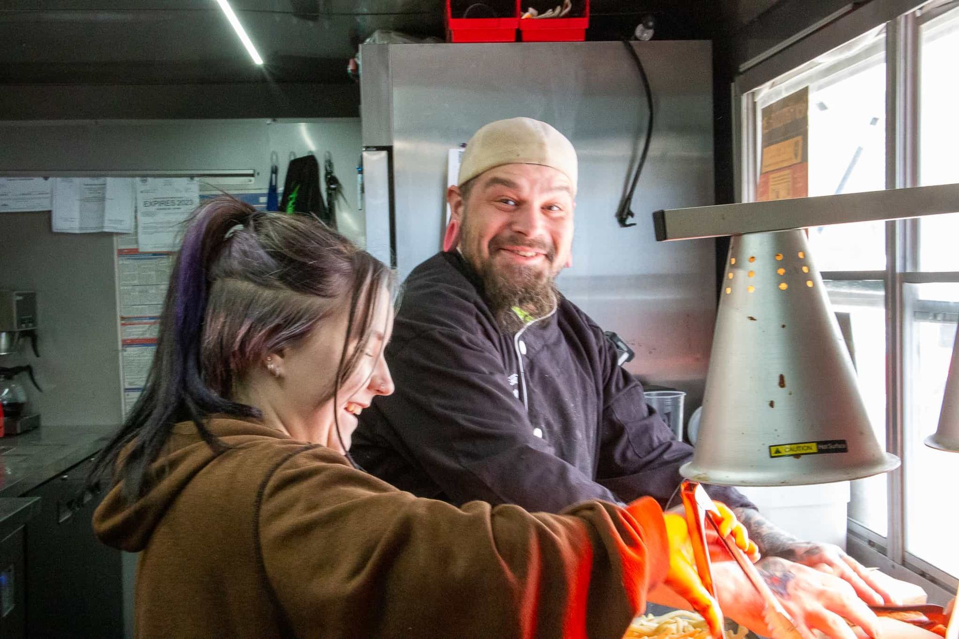 Two people, a man and a woman, smiling while working in a food truck.