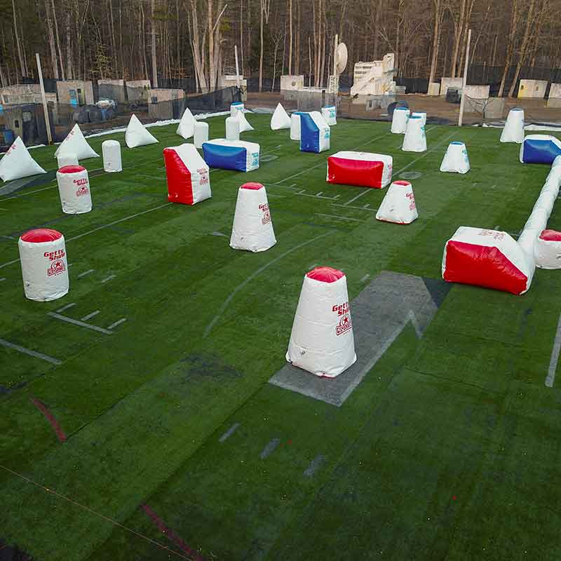 Paintball field with inflatable bunkers on artificial turf; trees in the background.