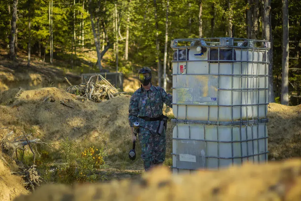 People playing paintball in a wooded area, with teepee-like obstacles for cover.