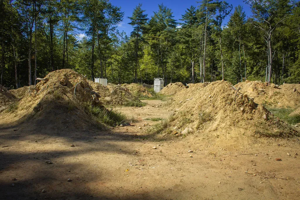 Teepees in a forest, painted white with red trim. Firewood and trees surround the camp.