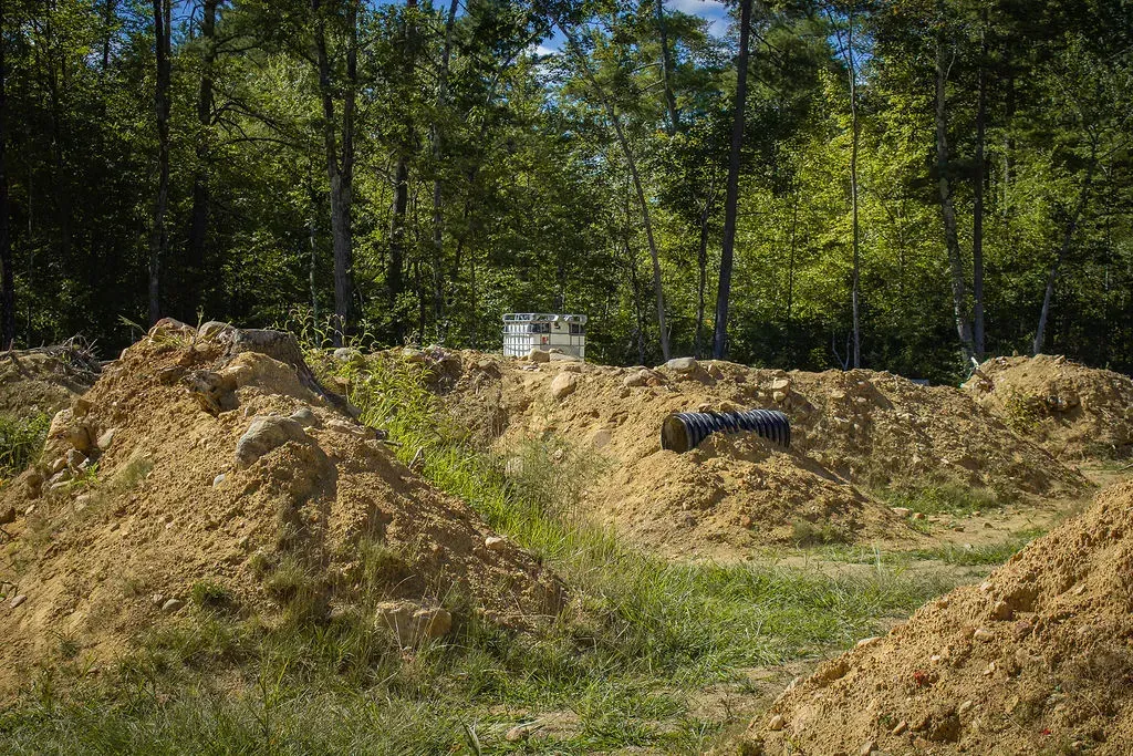 Three red and white teepees in a forest clearing, surrounded by trees and logs.