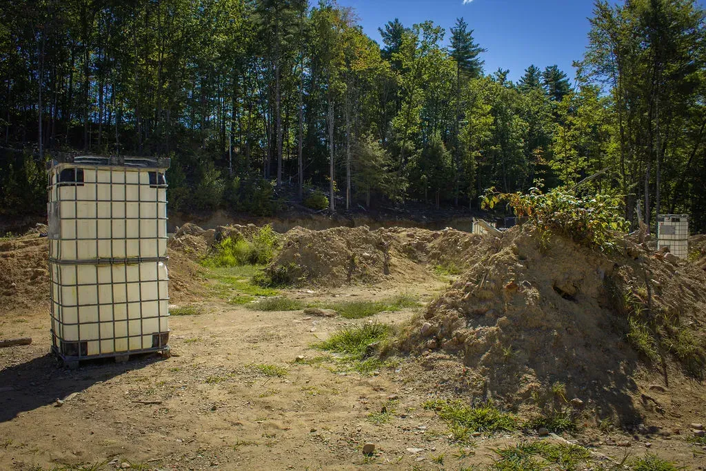 Two wooden teepees painted white with red trim in a wooded area. One has a circular window.