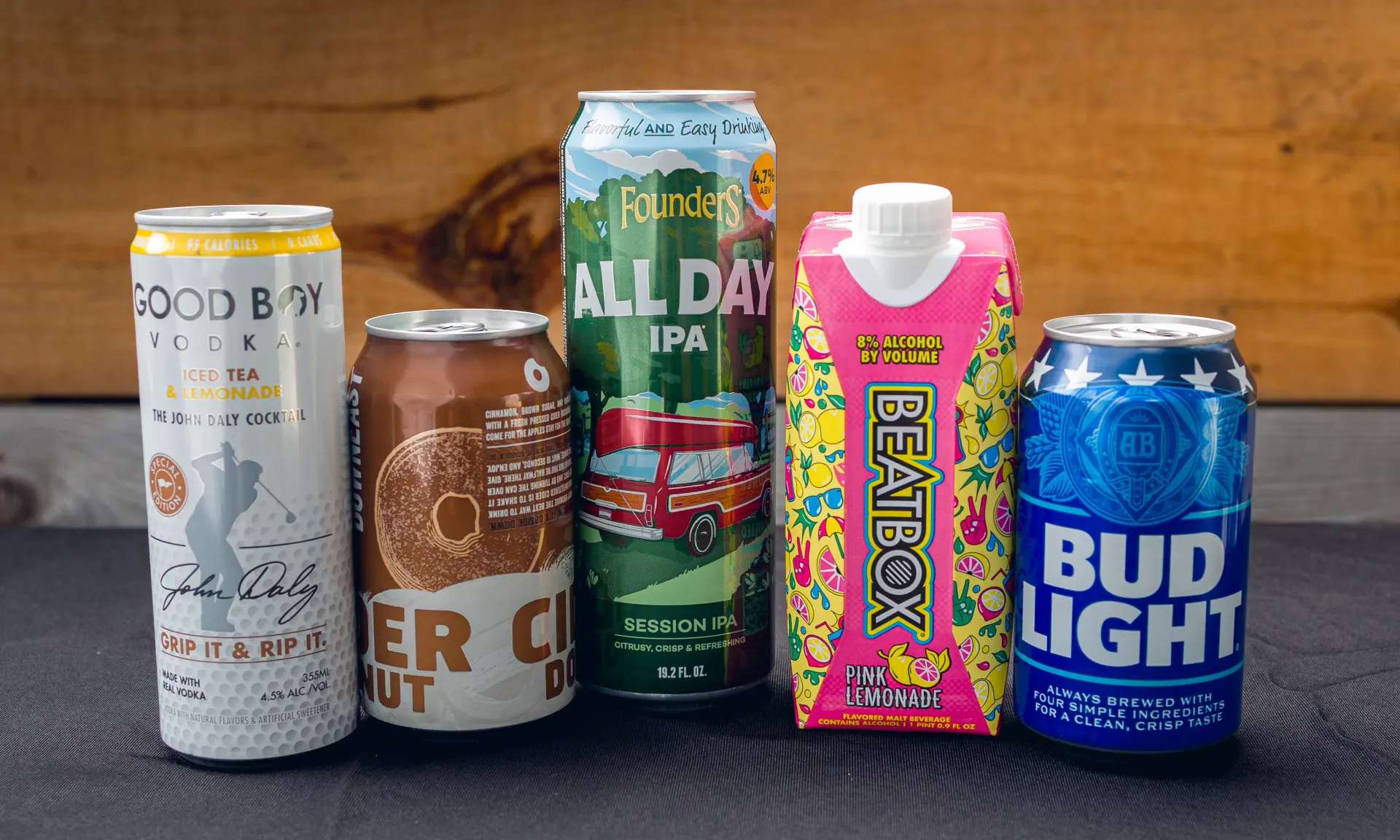 Five beverage containers: a can of Good Boy seltzer, a coconut beer can, IPA can, juice box, and Bud Light can.