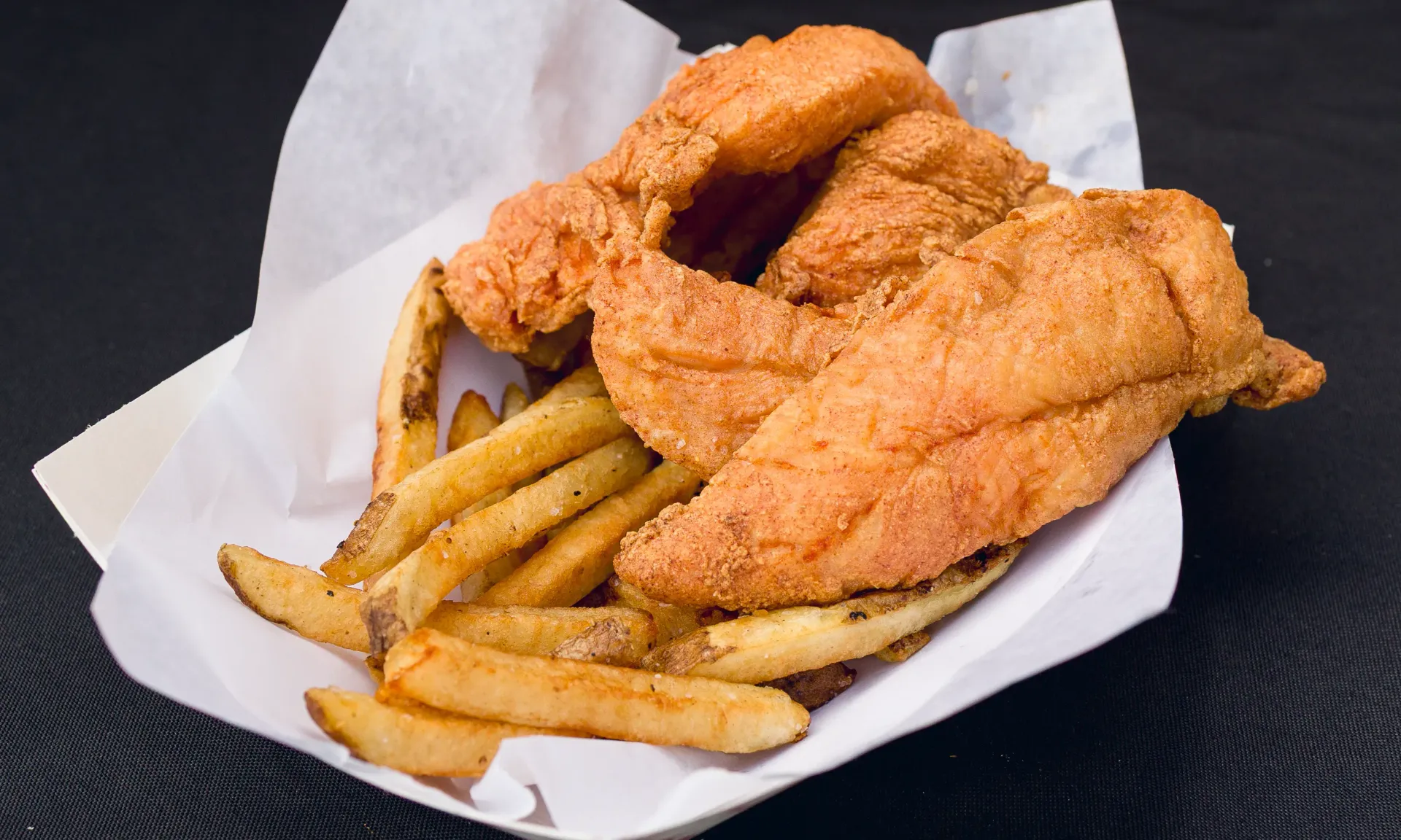 Fried fish fillets with fries in a paper tray.