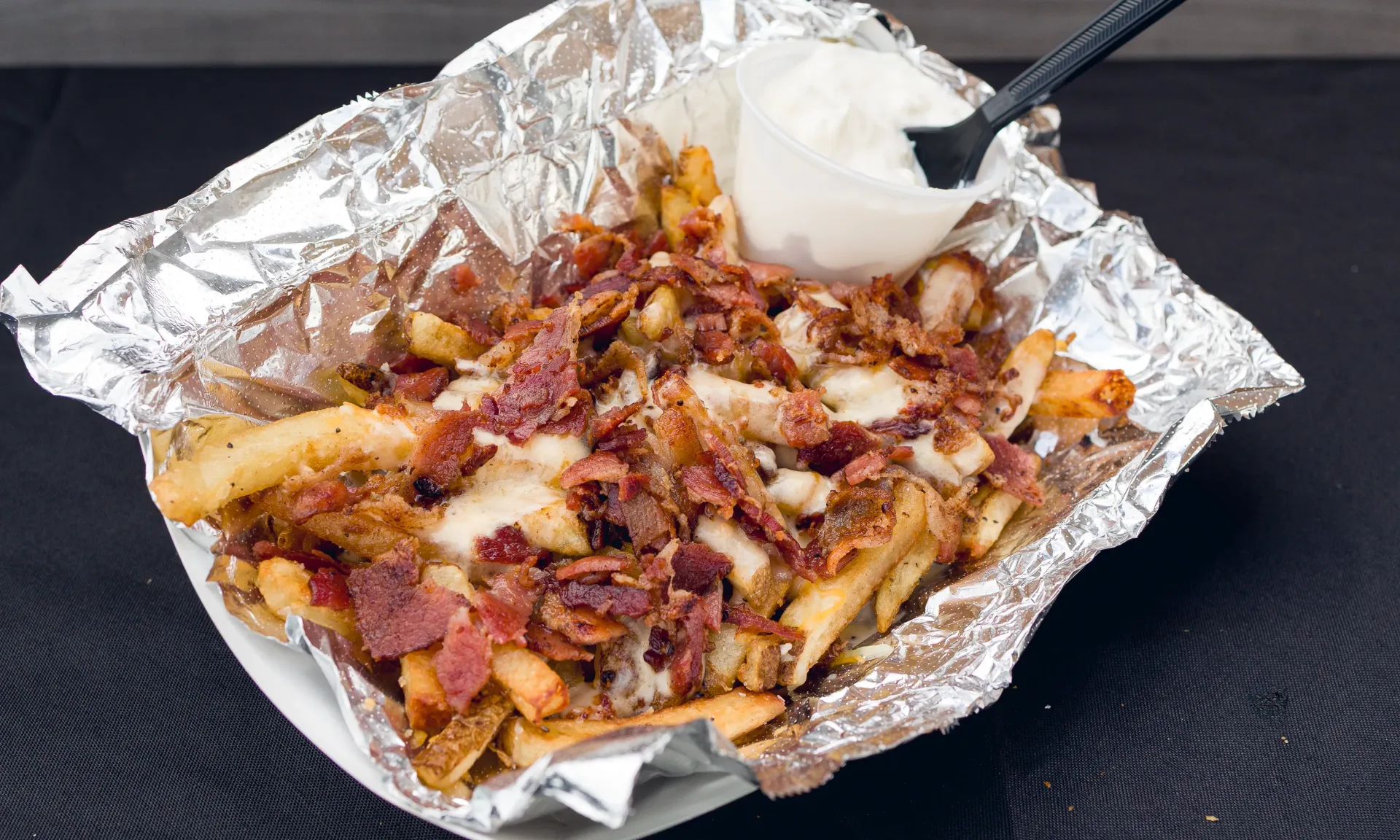 Fries topped with meat and cheese in foil, served with a side of white sauce.