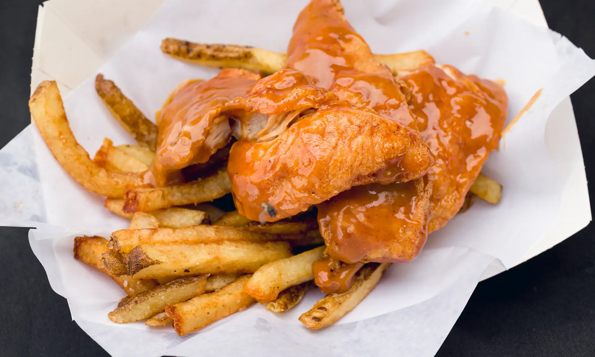 Fish and chips with orange sauce in a paper container.