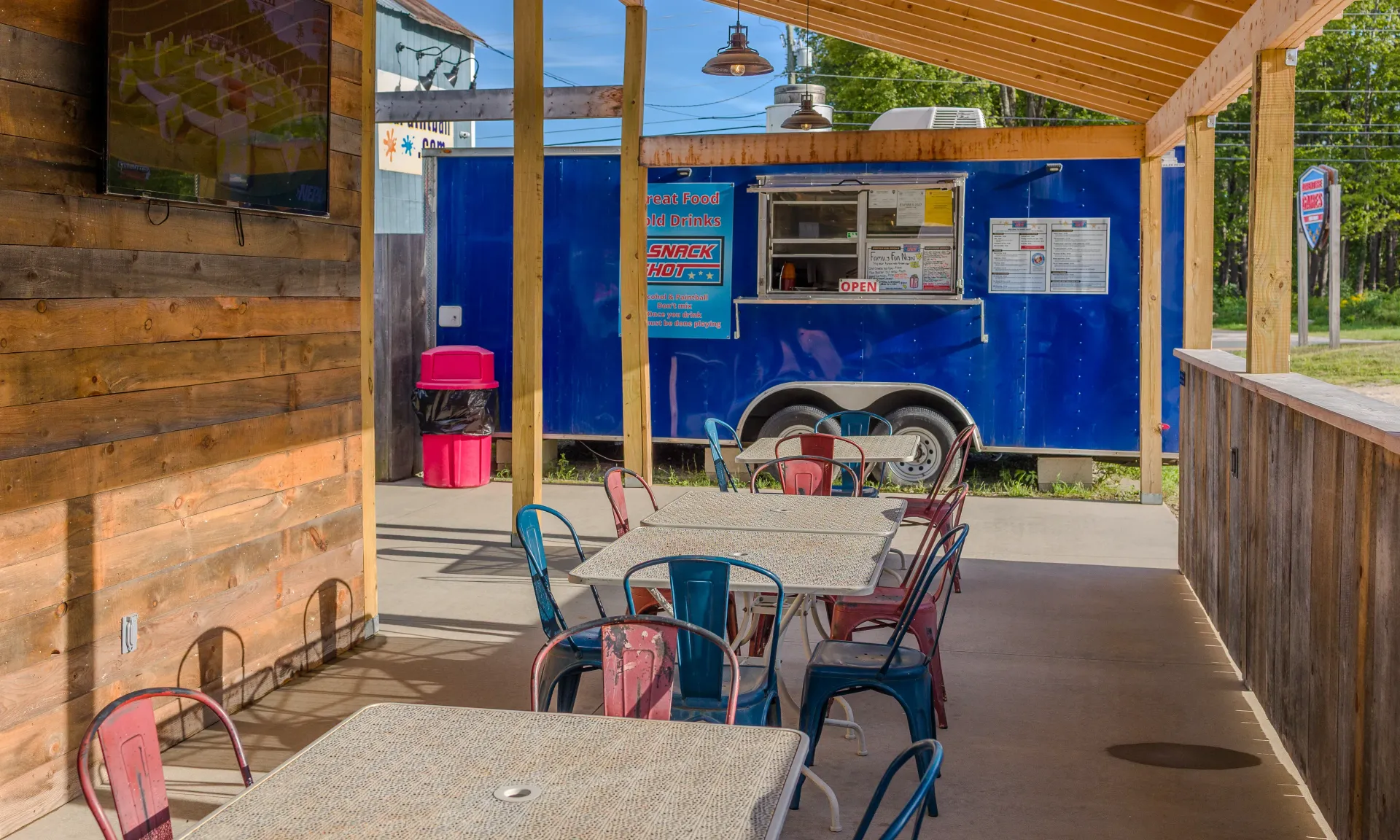 Outdoor seating area with colorful chairs, a blue food truck, and a wooden canopy.