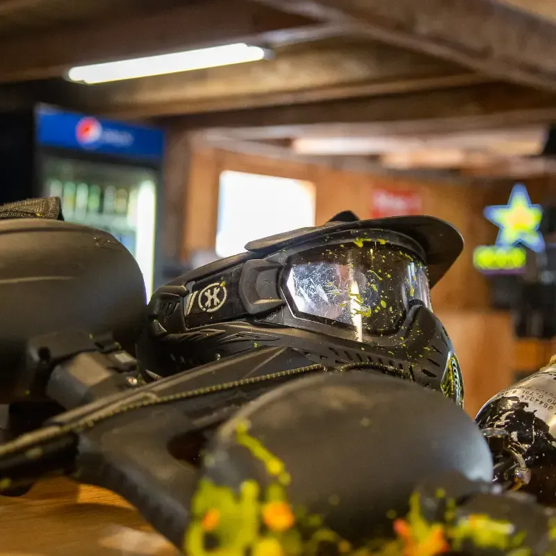 Paintball gun and mask splattered with yellow paint, indoors.