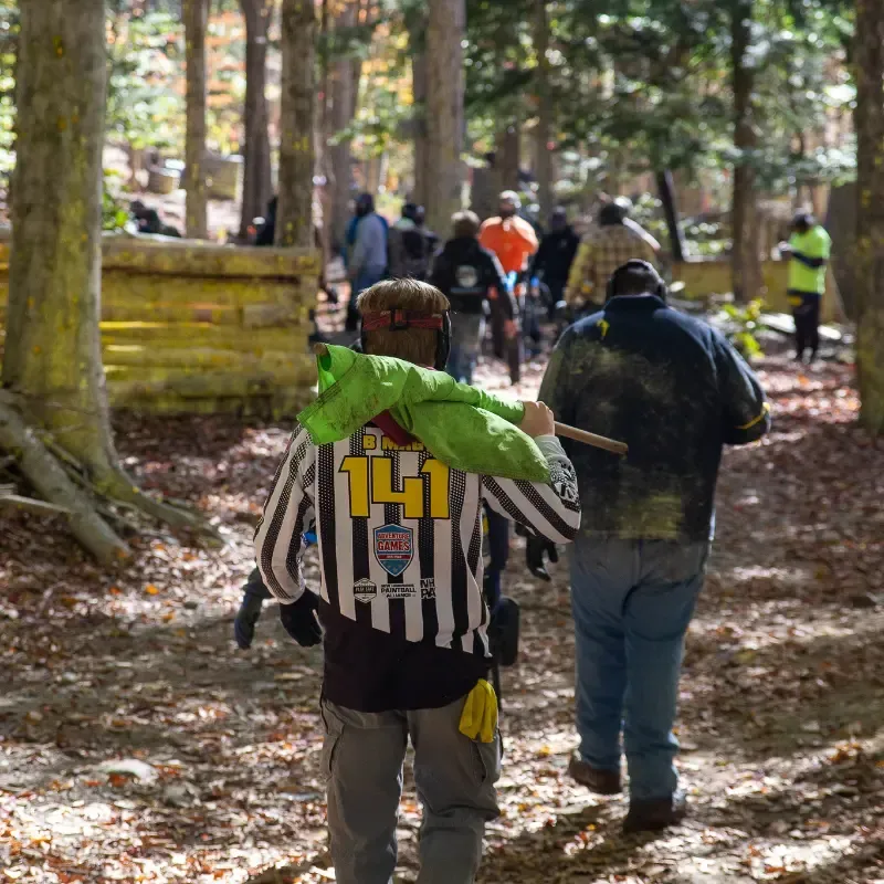 People in paintball gear walking in a wooded area, some with paintball markings.