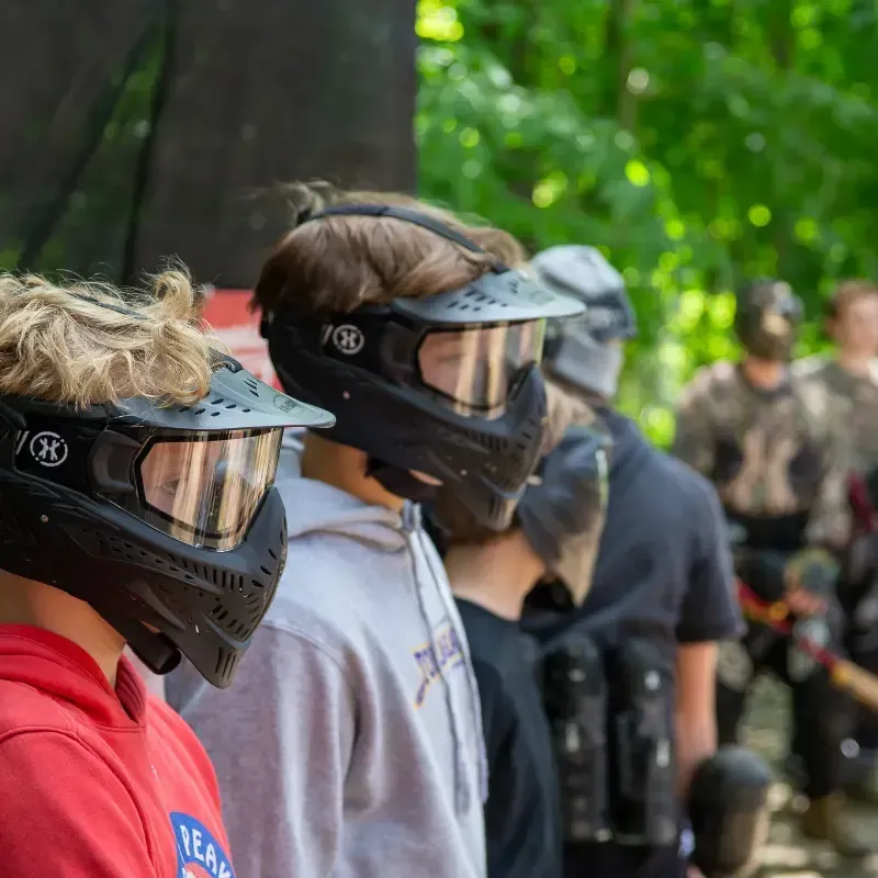 People in paintball masks and gear lined up outdoors, ready to play.