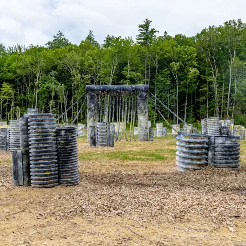Paintball field with gray bunkers, trees in the background, and a cloudy sky.