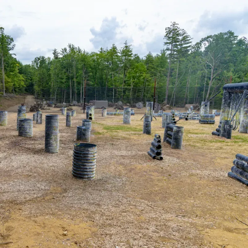Paintball field with tire and bunker obstacles in a wooded area under a cloudy sky.