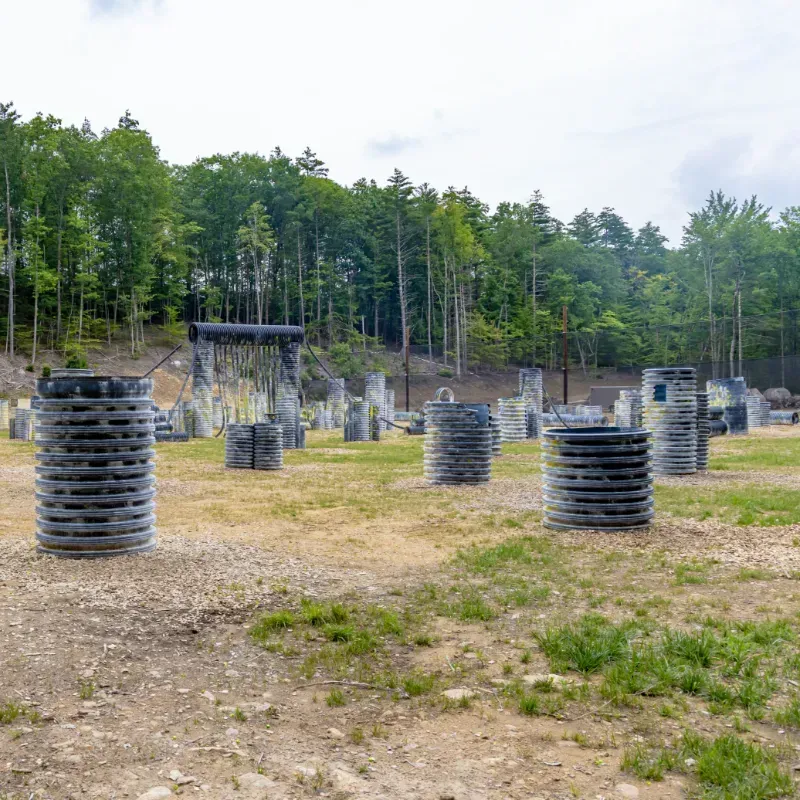 Paintball course with tire and bunker obstacles in a field, trees in the background.